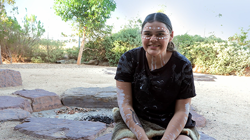 Jedah wearing Aboriginal Body Art outdoors infront of a fire put while discussing how the Victorian education system be improved for First Peoples