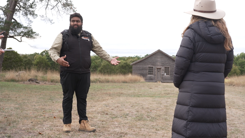 Commissioner Hunter listening to a talk about Lake Condah Mission with the mission in the background