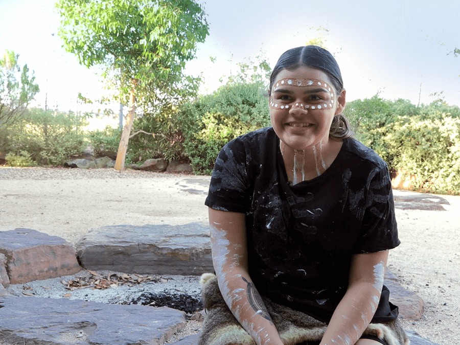 Jedah wearing Aboriginal Body Art outdoors infront of a fire put while discussing how the Victorian education system be improved for First Peoples