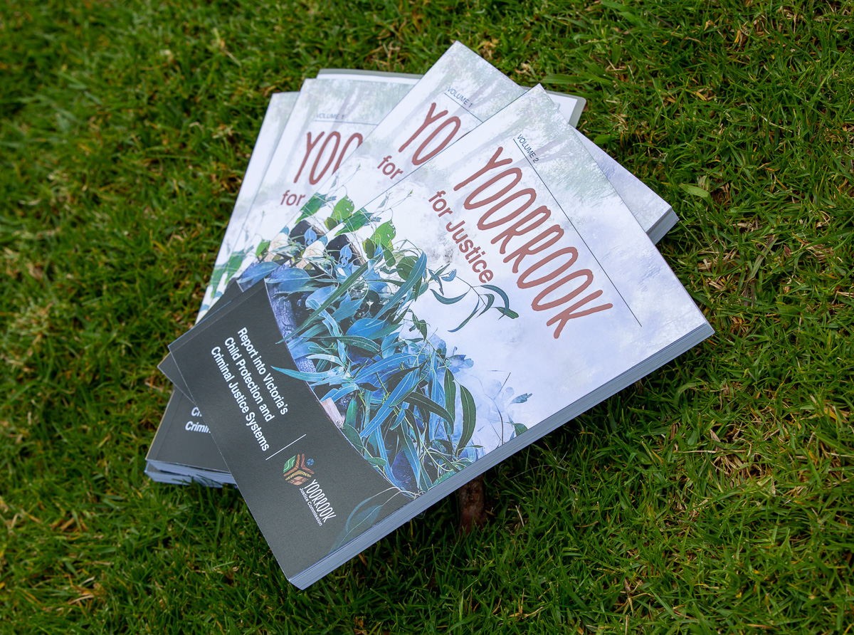 4 copies of the Yoorrook for Justice report placed on top of grass at the Kings Domain monument in Narrm