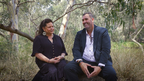 Aunty Jill Gallagher and Commissioner Travis Lovett yarning next to the Yarra River